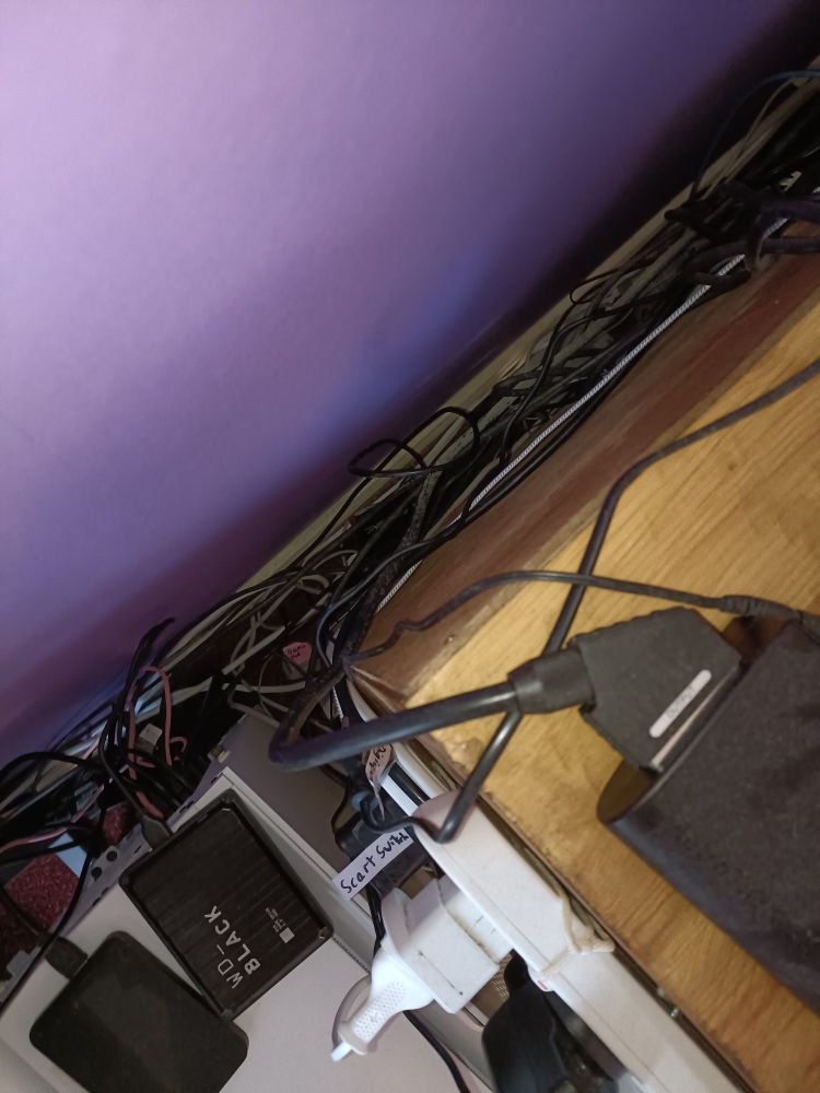 Bird's-eye view of a TV stand with a collection of plugs, cables, hard drives and video processors all over the place.