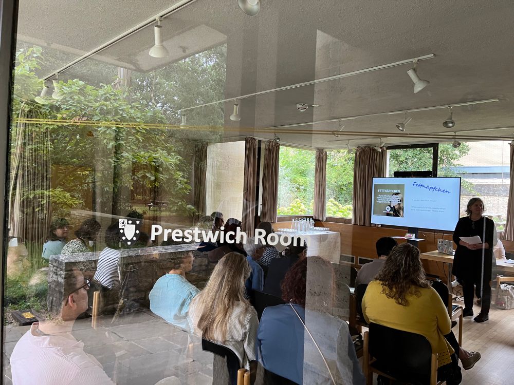 A classroom photographed from outside through the window with the words “Prestwich Room” written on the window pane