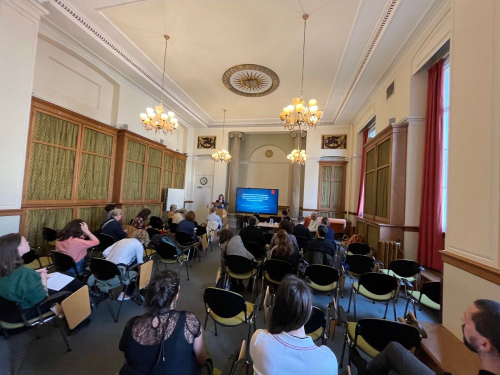 Classroom seen from the rear with the backs of the audience’s heads visible and a speaker at the front of the room facing the camera 