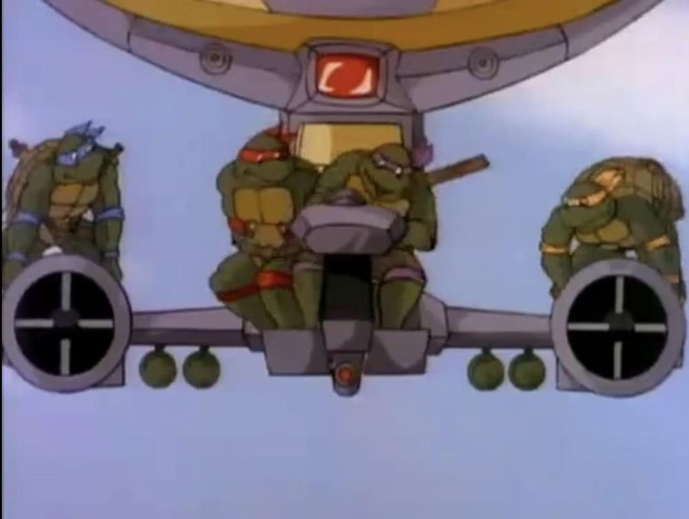 front on image of the 80s tmnt in the turtle blimp, the big zeppelin part of it mostly offscreen, donatello in the seat with raphael wedged in next to him side saddle, almost standing, leonardo & michelangelo riding the thruster thingies(?) like bikes