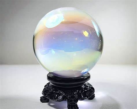 the first image search result for the term crystal ball

ball(centred in frame) seems clear/uncoloured but iridescent like an oil slick under a car & the link said insectsinresin.com, so probably it's made of resin

the base the ball is on(it's on a base) is black & kinda ornate, the background is white or light grey and indistinct except for a corner across the sort of horizon of the image