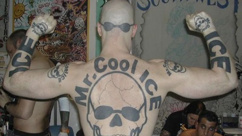 MR COOL ICE.  okay it's a guy standing with ihs back to the camera. He is shirtless and has a skull wearing sunglasses on his back, with MR COOL ICE above it.  The guy also has sunglasses tattooed on the back of his shaved head, and ICE tattooed on both forearms as well as a skull on each hand, and further skulls with MR COOL ICE above them on his shoulders