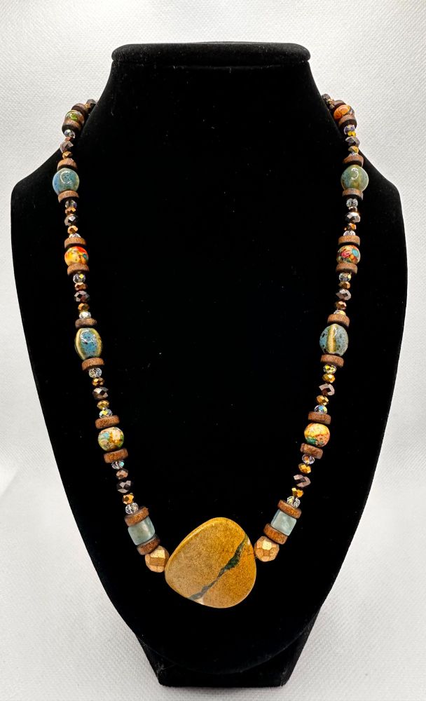 A gorgeous multicolored necklace with an unidentified gemstone centerpiece (I believe it's a wavy piece of jasper personally - it's a tannish brown with a grainy stone look and a stripe of deep green with bits of creamy white at the edges), ceramic beads, multicolored round beads, howlite cubes- and wooden/faceted spacer beads.