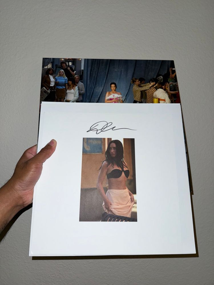 Photo of my hand holding up Demi Lovato’s It’s Not That Deep vinyl with a signed insert photo of her in front of it.