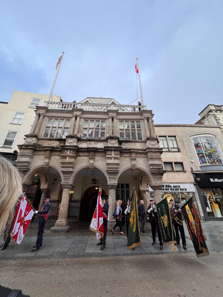 Picture of the Polish flag being raised on top of the guild Hall in front of the guild who are a row of flagbearers