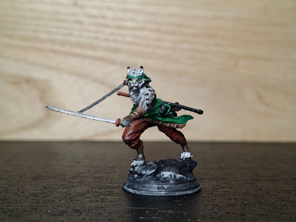 Painted miniature, snow leopard catfolk, wearing green headband, leather bracers, and brown trousers. He stands in lunge, holding two katanas - one in front, one behind him. Third katana, still in the sheath, is visible behind his back.
