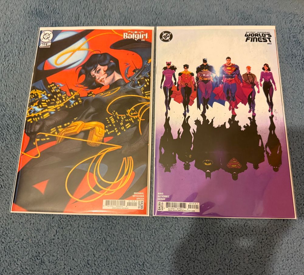 The covers to Batgirl #10 and World’s Finest #42 showing Batgirl with a city scape in her cape and Worlds Finest showing Catwoman, Robin Batman, Superman, Jimmy and Lois walking with a Bizzaro mirror image of the characters underneath 