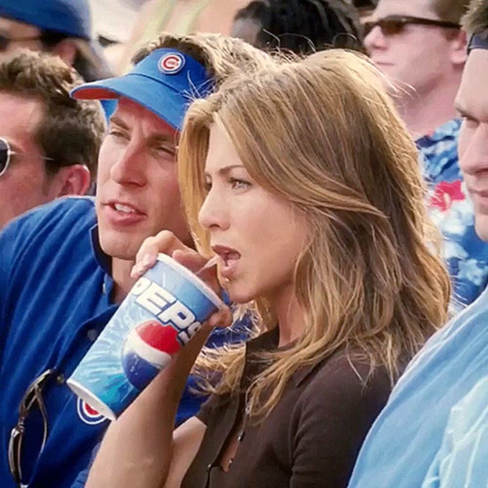 a woman is drinking a pepsi cup while watching a baseball game