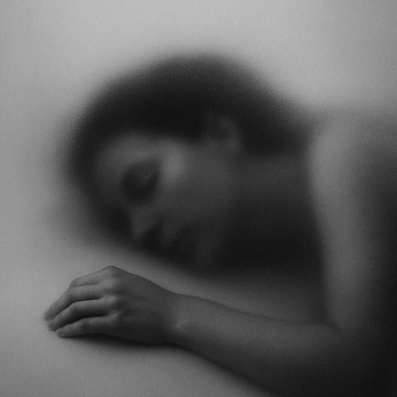 A black and white photograph shows the blurred silhouette of a sleeping woman behind a frosted surface. Created with GPT4o.