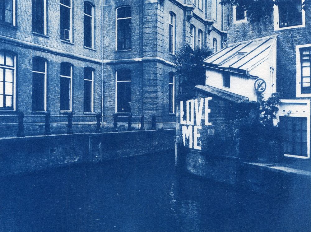 Cyanotype d'un canal amstellodamois et de ses bâtiments en brique qui l'entourent. Sur un muret, l'inscription Love Me.