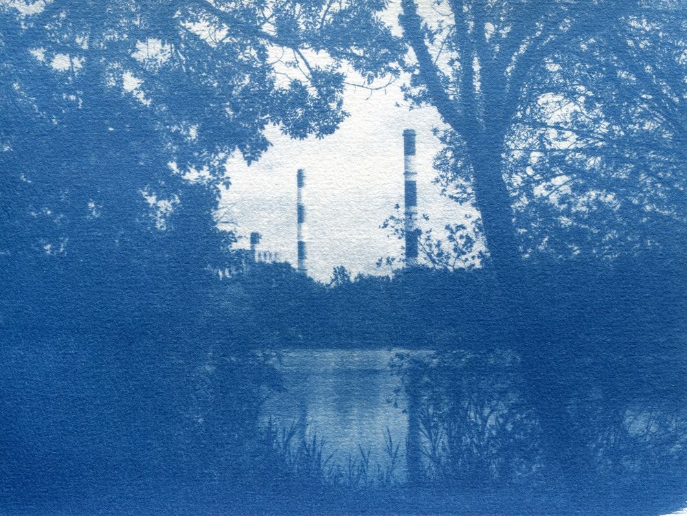 Cyanotype des cheminées de la central thermique de Cordemais qui se reflètent dans la rivière avec des arbres autour.