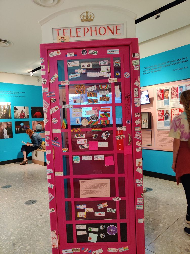 A pink British telephone box, covered in LGBTQIA+ positive stickers. This was an exhibit representing the stickers against hate movement in Oxford, part of the "Beyond the Binary: Gender, Sexuality, Power" exhibition at the Pitt Rivers Museum in 2022.