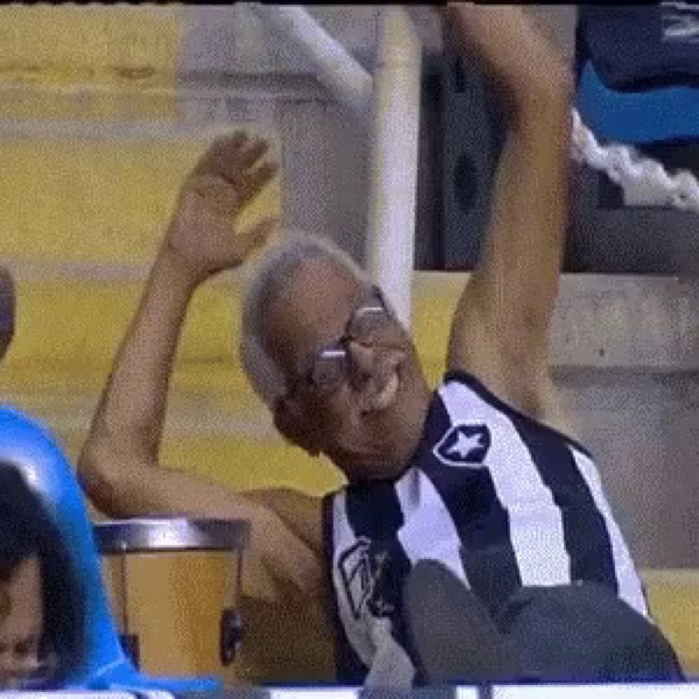 an older man wearing glasses and a striped shirt is sitting in a stadium with his arm in the air .