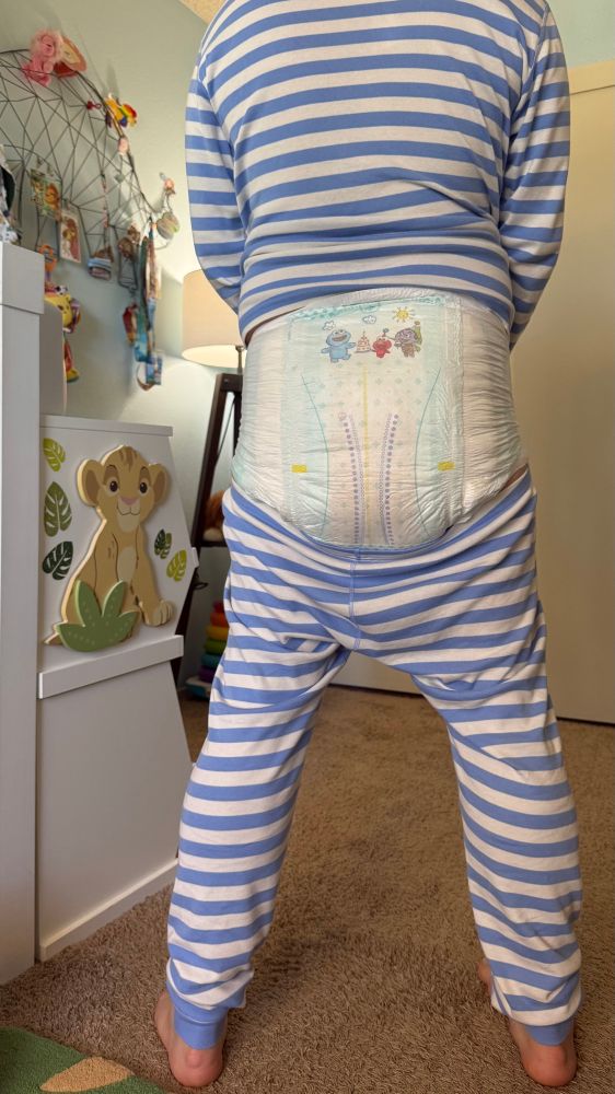 Junior in blue striped two-piece pajamas, tugged down to expose a huge disposable diaper with Sesame Street characters dancing on the waistband.  He’s standing in his nursery, just to the side of his change table.