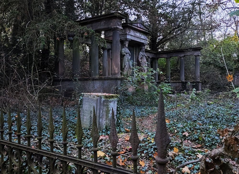 Ruinen mit Säulen und Skulpturen im vordergrund ein rostiger Zaun