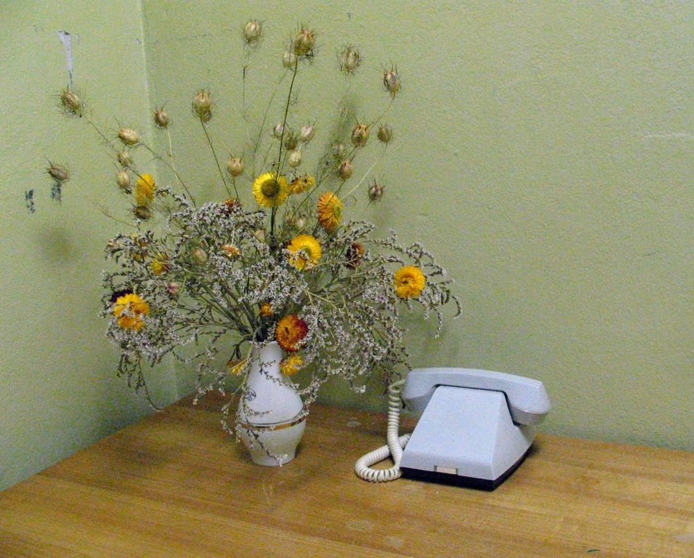 altes graues telefon ohne Tasten oder Wählscheibe daneben ein Blumenstraus in Vase