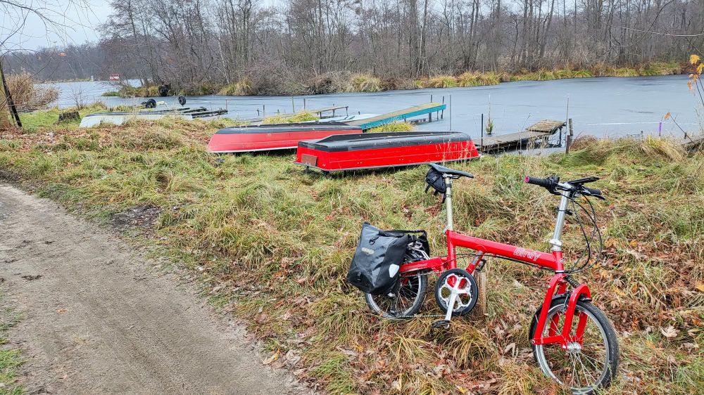 rotes Rad und rote Boote zwischen einem Feldweg und einem zugefrorenen See