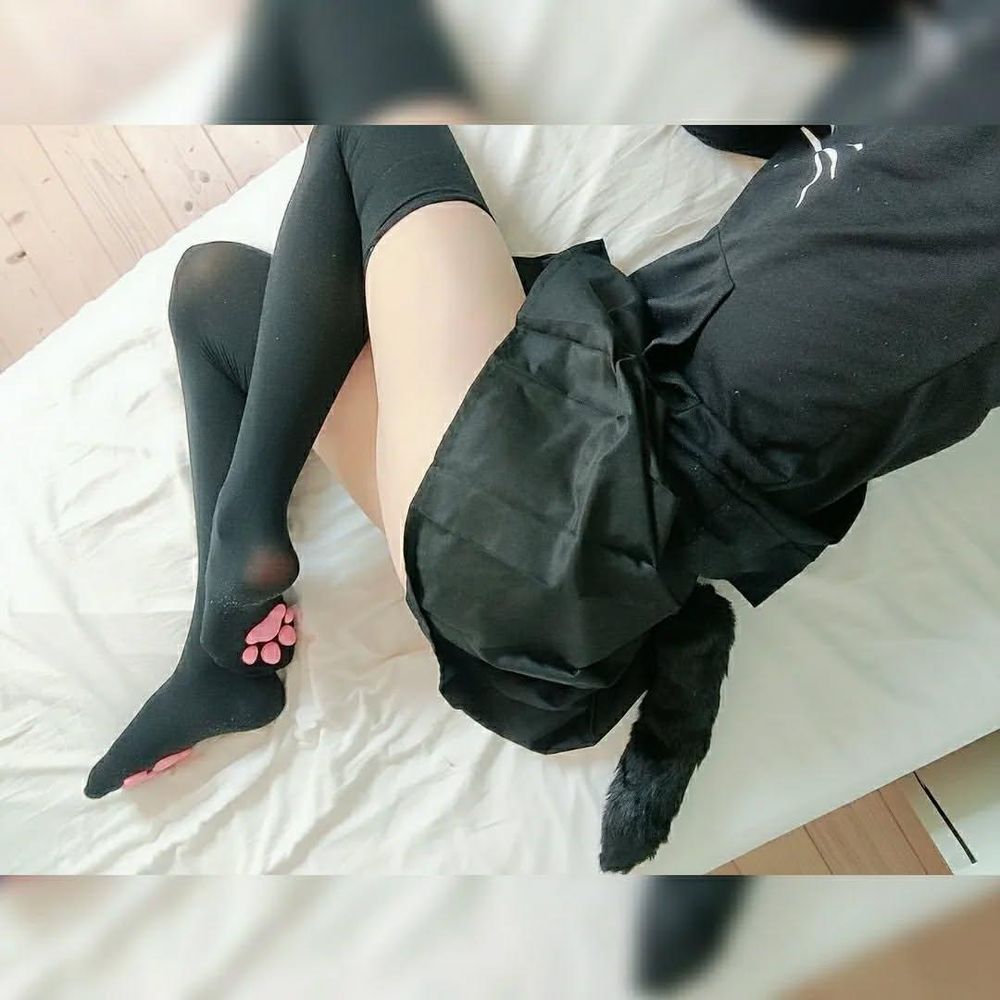 femboy laying down on his side wearing cat paw thigh highs, a black skirt a black tail and a black hoodie