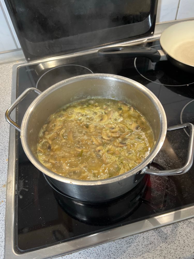 A stove with a pot that contains a boiling liquid. Its a risotto 