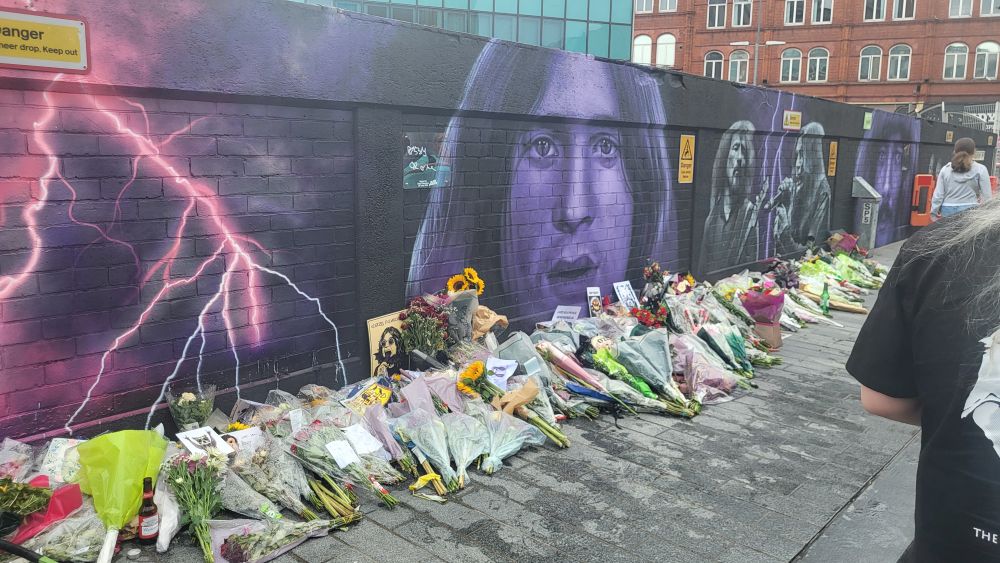 A brick wall adorned with flowers and graffiti of the Black Sabbath members