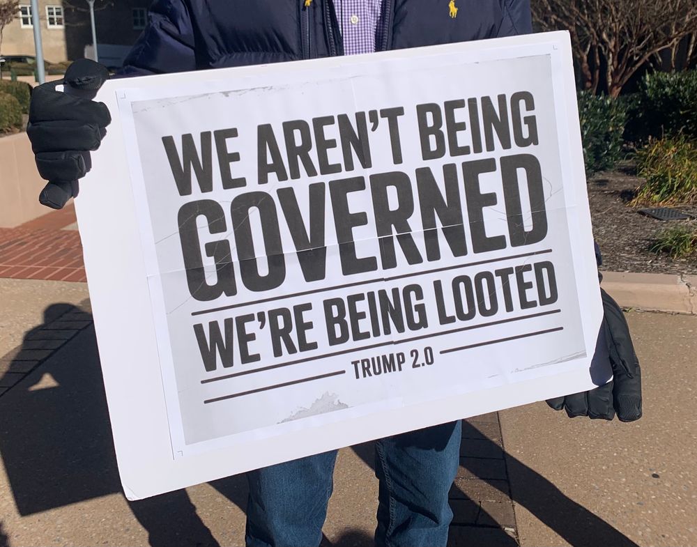 A sidewalk photo of a protest sign that reads “We aren’t being governed, we’re being looted.”