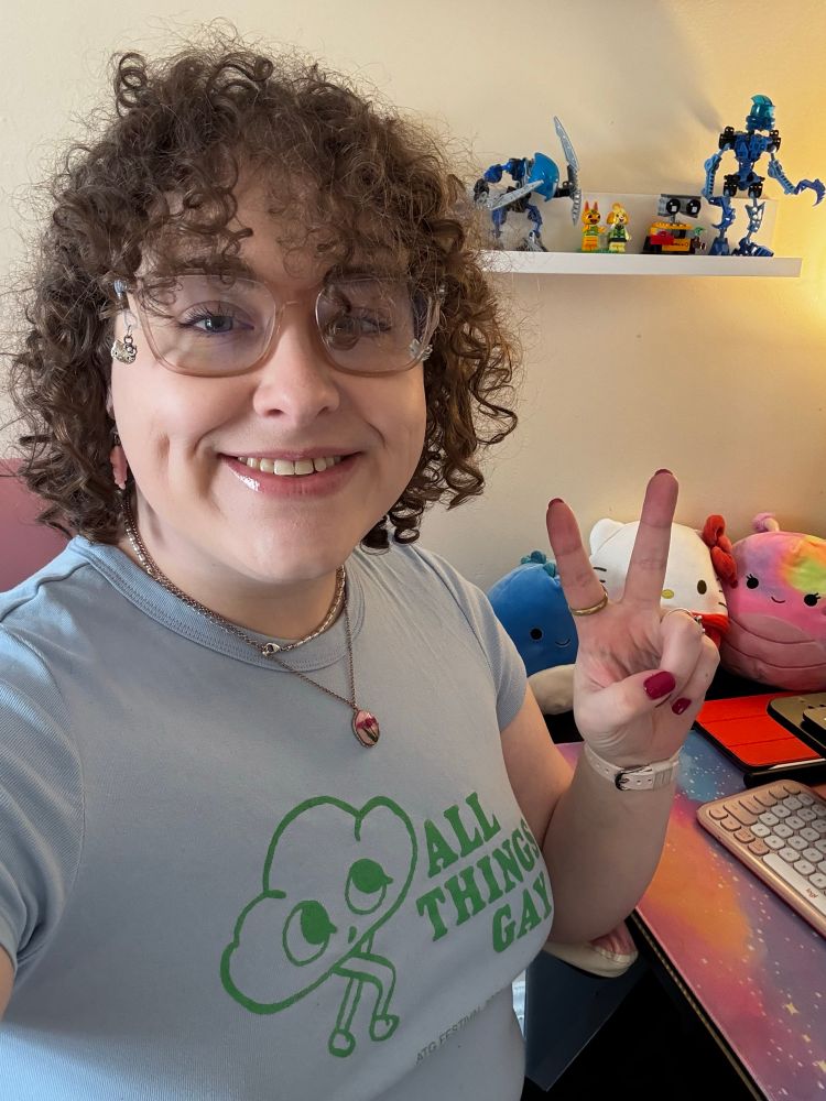 Maxie with light blue all things gay shirt throwing up the peace 