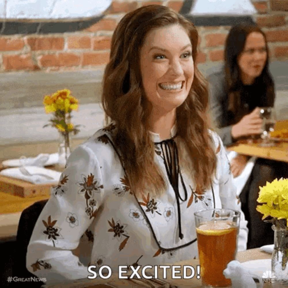 a woman is sitting at a table with a glass of beer and smiling while saying so excited .