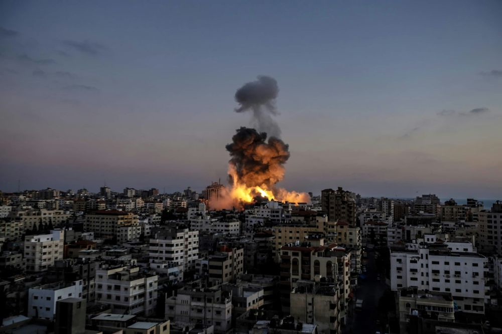 An explosion in a building in Gaza. Smoke and fire rise above a city full of buildings. 

