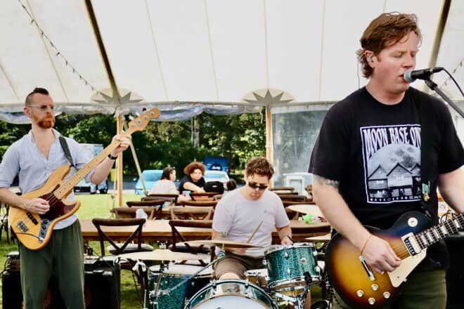 The band Dad Bod and the Father Figures playing music in a tent. 