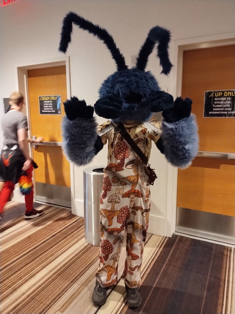 A dark blue ant partial fursuiter with a mushroom printed onesie