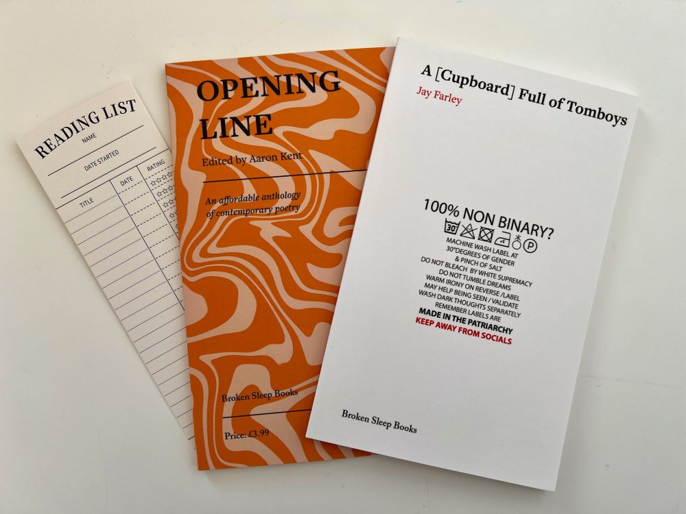 A photo of two books published by Broken Sleep books and a bookmark fanned out on a white background. The books are the anthology 'Opening Line', edited by Aaron Kent which has a swirly orange and peach coloured cover, and 'A [Cupboard] Full of Tomboys' by Jay Farley, which features a poem presented/shaped like a washing label, with the words in larger letters at the top '100% NON BINARY?'. The bookmark is a blank reading list with columns for 'title', 'date started' and 'rating'.