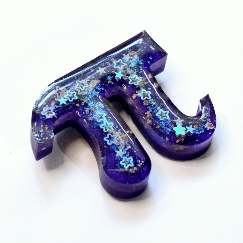 A Pi symbol shaped brooch made from layered resin in different shades of purple with tiny iridescent stars on the surface
