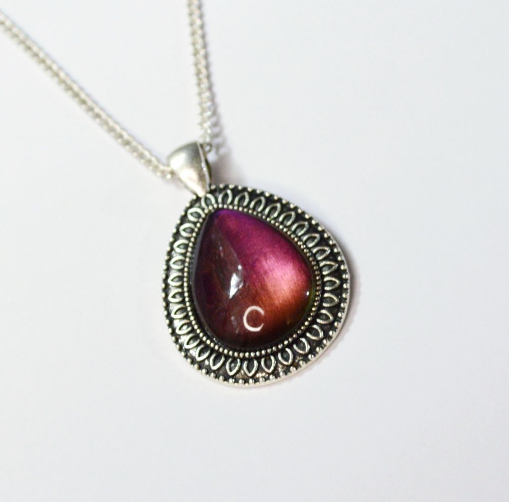 A tear-drop shaped silver pendant with a fancy silver frame and a burgundy cabochon. 