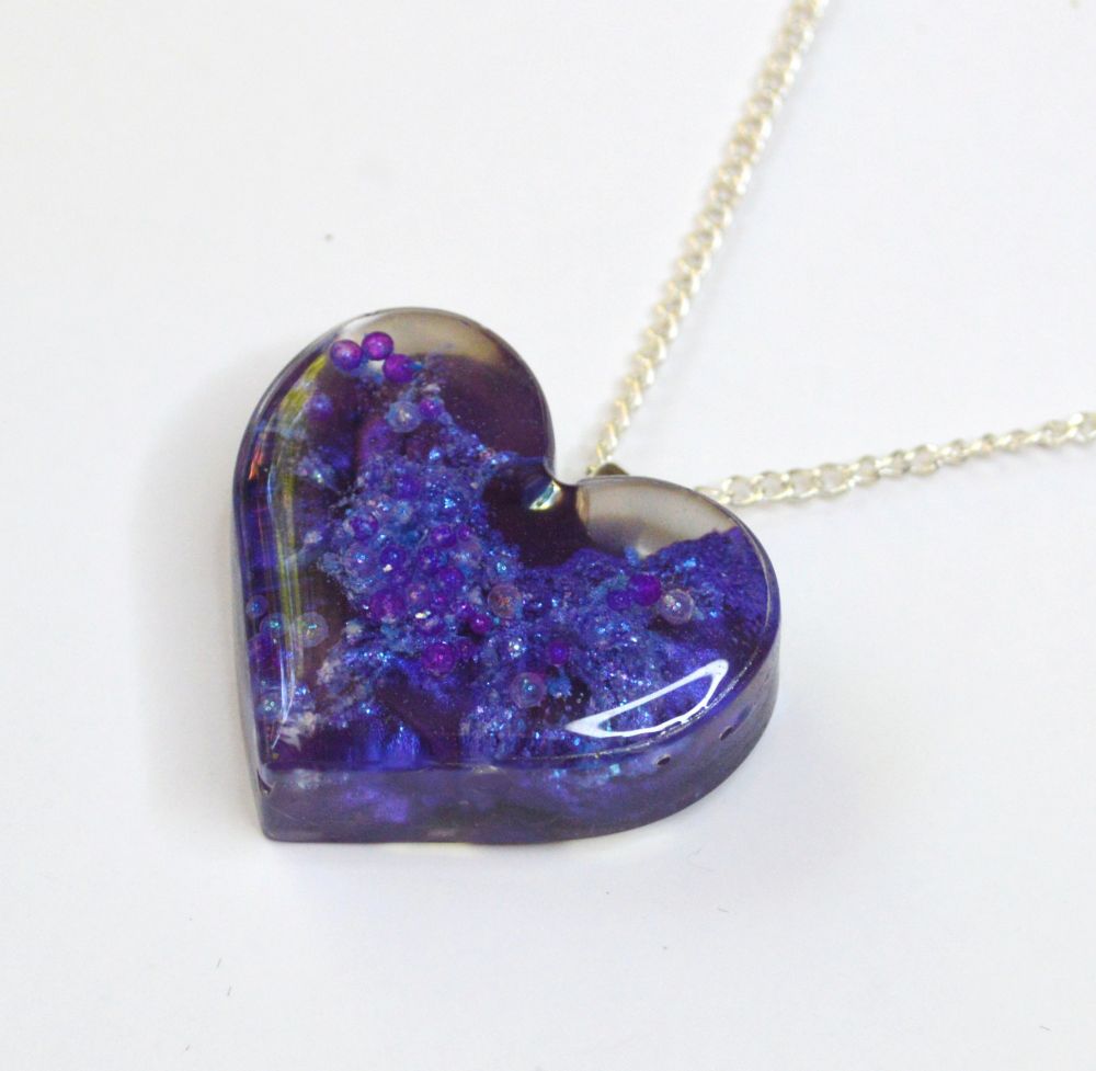 A heart pendant made from chaotically layered resin and pigments in various shades of purple. 
