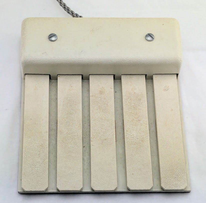 The keyset is an input device with five long, flat keys, similar to piano keys but thinner. The device and the keys are beige. A braided wire cord exits the device at the top.