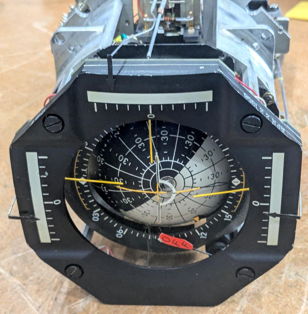 The FDAI is an octagonal instrument with a rotating ball in the center. The ball is half black and half white, with numbers and lines on it to indicate angles. Three yellow needles direct the astronauts with the desired motion. Three arrow scales on the sides show the spacecraft's roll rate in the three axes. An orange flag labeled "OFF" is visible.
The cover has been removed from the FDAI so some of the internal components are visible. 