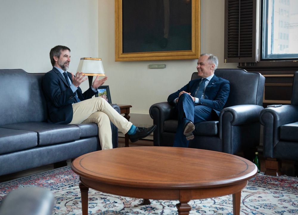 Le ministre Steven Guilbeault assis sur un fauteuil (gauche) discute avec le premier ministre Mark Carney (droite).