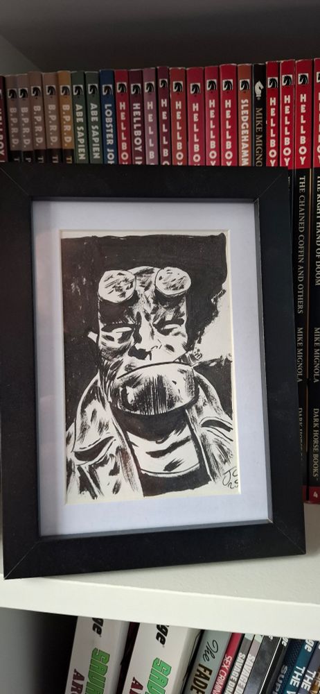 Framed ink Hellboy bust in front of a collection of Hellboy comics.