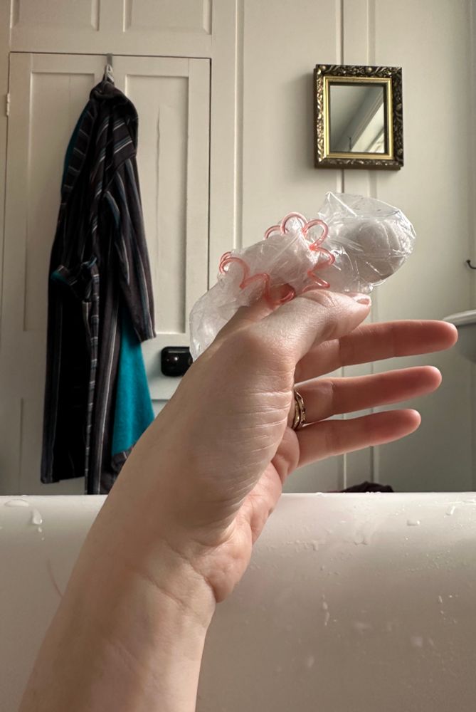 A arm rests on the edge of a bath. The index finger is bandaged and wrapped in a plastic bag, held in place with a hair bobble.