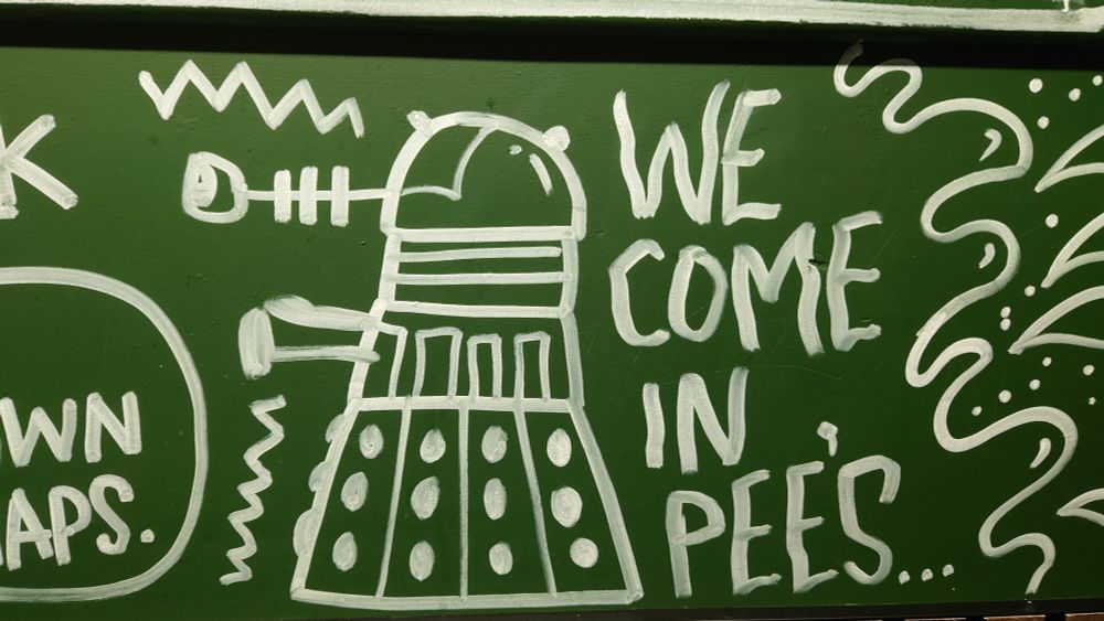 graffiti type artwork, white paint on green background, of a dalek and the message "we come in pee's" - and yes we'll forgive that extraneous apostrophe 