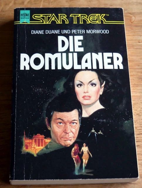 Buchcover, Titel: "Die Romulaner", darauf zwei Portraits eines menschlichen Mannes und einer romulanischen Frau (mit spitzen Ohren), darunter in klein nochmal zwei Leute, die vor zwei Ramschiffen wegrennen, im Hintergrund ein Gebäude