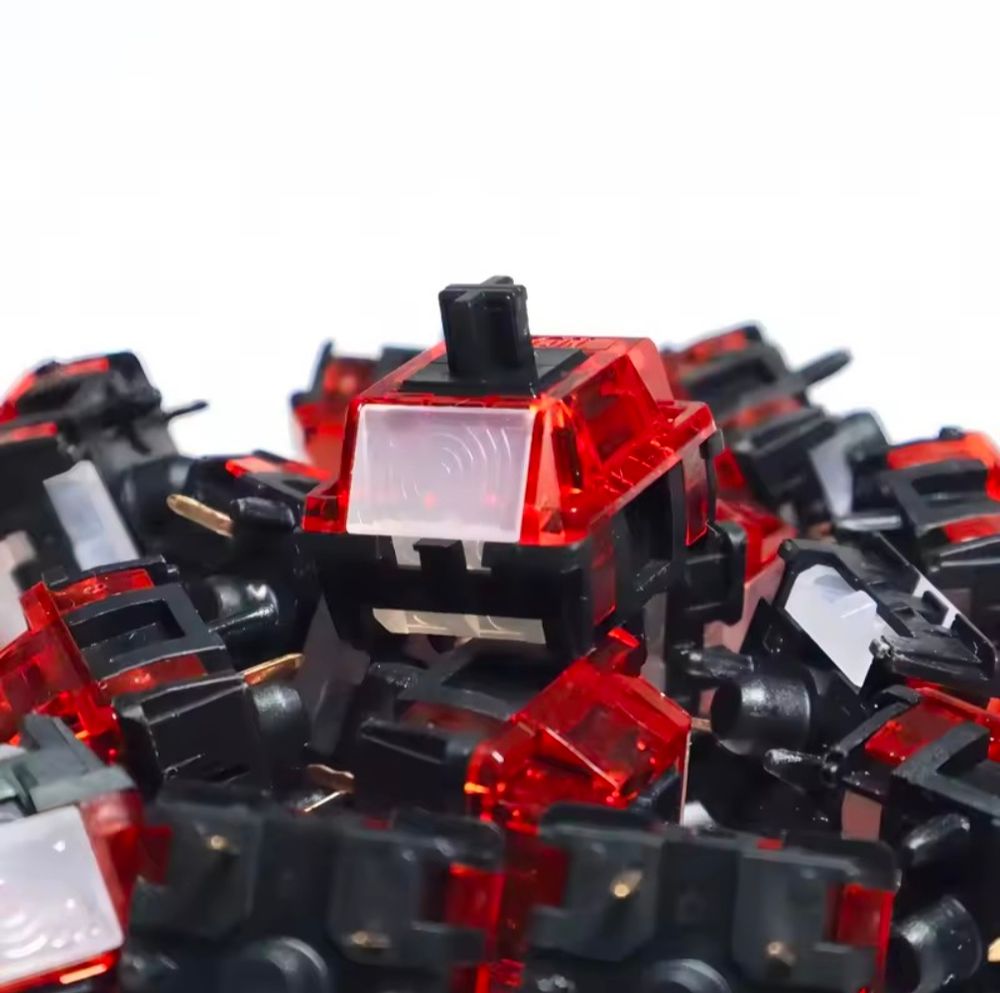 Geonworks MX style key switch sitting on a pile of more switches. It has a transparent red upper body, black base, black MX connector, and a white window for LEDs