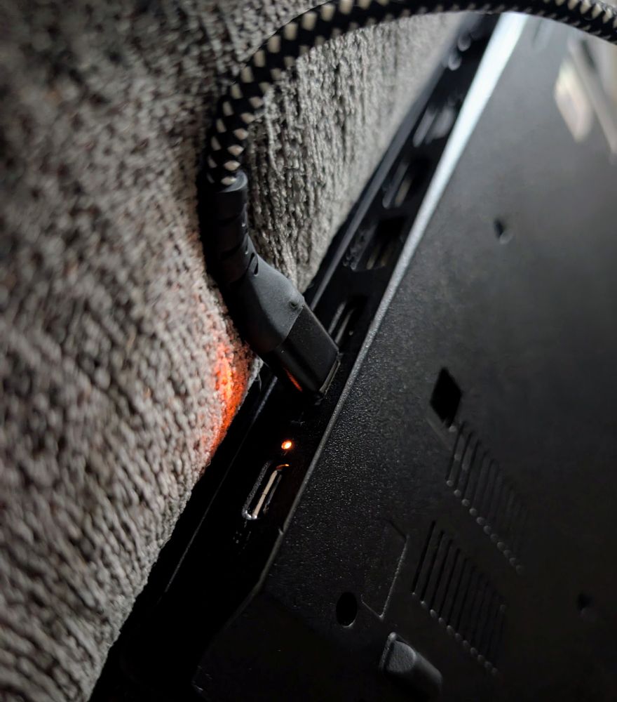 Thinkpad with USB C cable wedged in port, laying against couch. One of the few ways I'm able to successfully charge it.