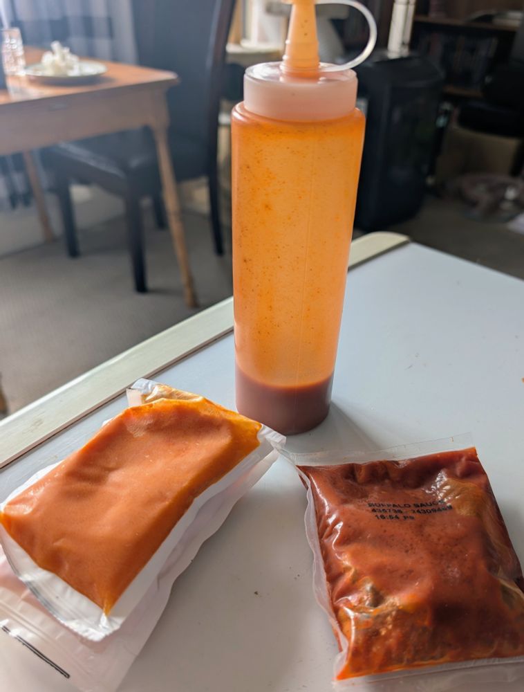 Some example pouches of buffalo sauce that comes with frozen chicken wings and nuggets. I place a couple pouches in room temperature water to defrost, then pour them into a sauce bottle from the dollar store. The bottle makes it easy to add to anything.