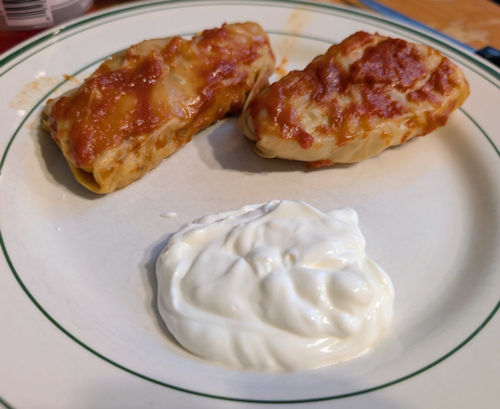 Two cooked cabbage rolls, tomato on top, with a side of sour creme
