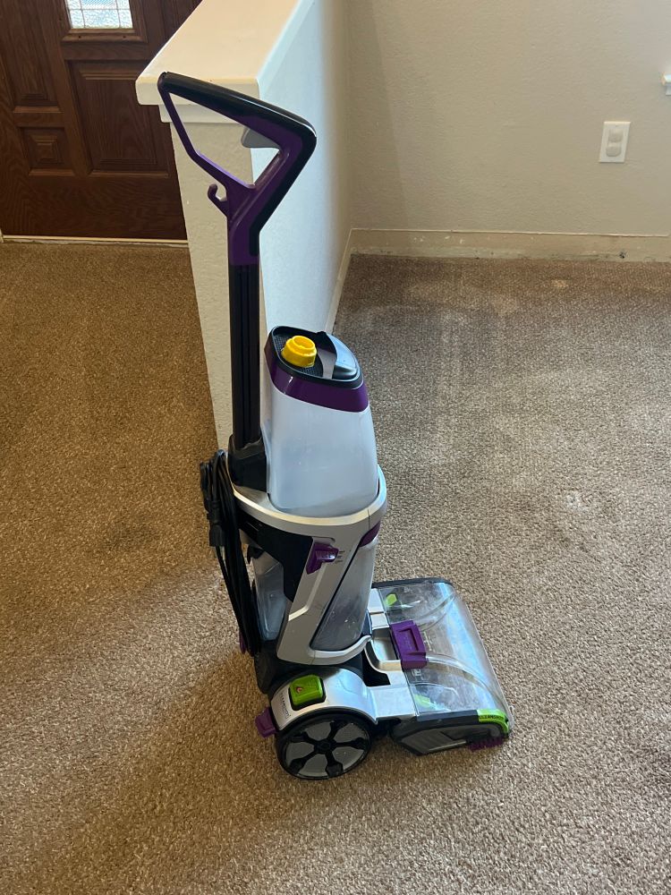 An upright carpet, cleaning machine sits in a room, being celebrated for five years of service having finally stopped working. 
