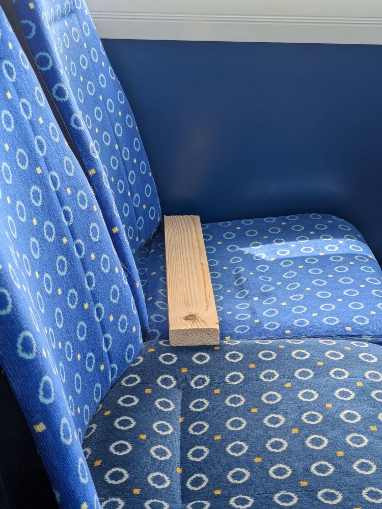 A plank of light-colored wood laying on a blue bus seat.