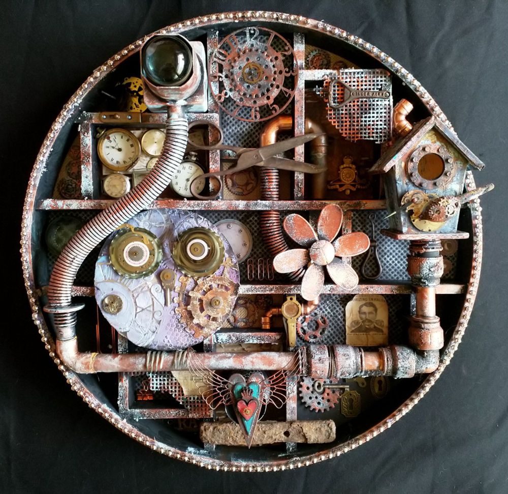 A large circular frame with small compartments. Each compartment is filled with oddities like clock parts, scissors and small pictures. It looks rusty and industrial with copper piping and tubes. On the left, sitting on a copper pipe is an owl made from a vinyl single record; his feet are forks and his eyes are cogs. Above, to the right is a rusty bird box with a bird sitting on it made from clock parts and a spoon.