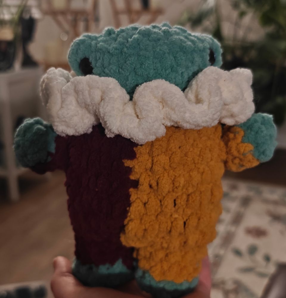Crochet teal frog with mustard and maroon jester suit with cream ruffle around the neck 
