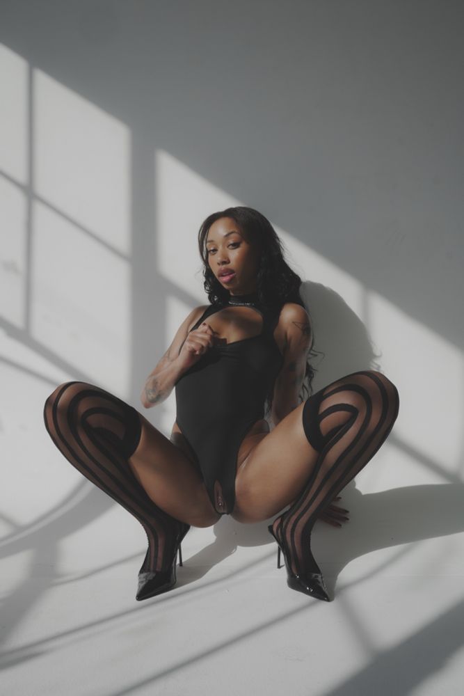 shiksa wears a black crotchless body suit, striped stockings, and heels as she squats and spreads her legs open exposing her pussy